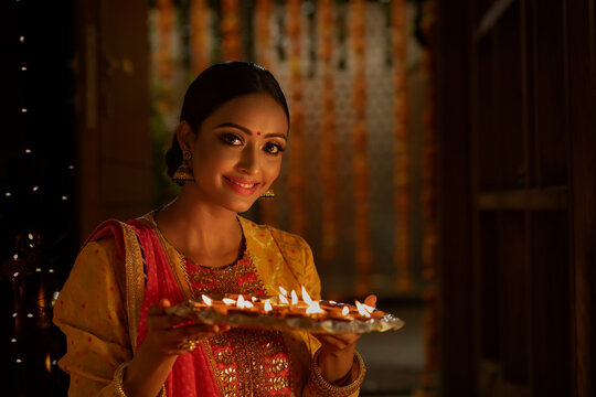 PORTRAIT OF A HAPPY YOUNG WOMAN POSING WITH DIYAS IN FRONT OF CAMERA	