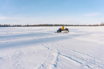 a large empty area covered with snow and snowmobile tracks. A guy in a yellow jacket rides a snowmobile