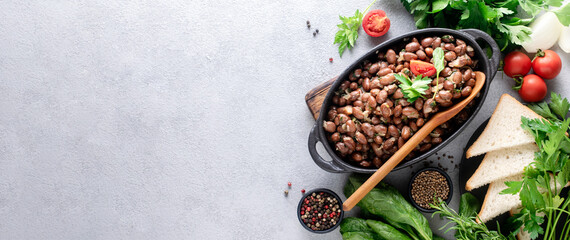 Baked beans with spinach and onions in a black bowl on a gray background with copy space. Banner