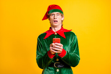 Photo of man hold cellphone puzzled upset face look camera wear elf velvet green costume headwear specs isolated yellow color background
