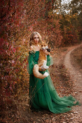 Model in a green dress with a red fox in the autumn forest