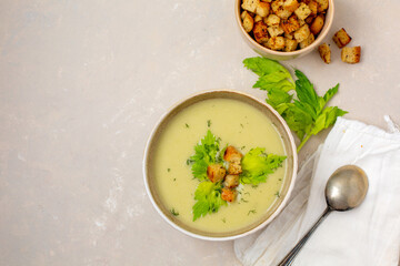 Top View of Bowl of Creamy Celery Soup with Croutons, Celery Leaves, and Dill with a Bowl of Croutons on a Light Tan Background