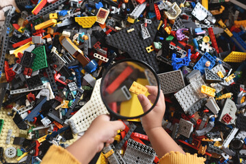 Fototapeta premium little child hand holding magnifying glass looking on a plastic toy block. Concept of creativity and childhood