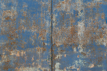 The wall is made of old blue metal panels. There is rust, layers of old paint are visible. There is a joint of sheets in the middle of the frame. Background. Texture.