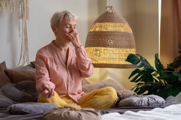 Senior woman practicing yoga at home, making Alternate Nostril Breathing exercise, nadi shodhana...
