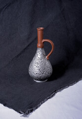 Vintage clay bottle with brown neck and silver textured painting on black and white fabric...