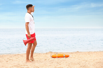 Handsome male lifeguard with megaphone at sandy beach