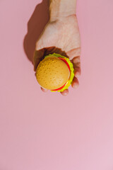 Burger in hand on  pink background. Creative concept. Plastic pop art flat lay style. Minimalism