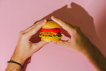Tasty burger in two hands on pink background with shadows. Creative concept. Plastic pop art flat lay style.
