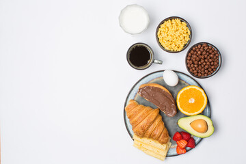 Milk, black coffee, croissant, toast with chocolate cream, flakes, fruits on breakfast