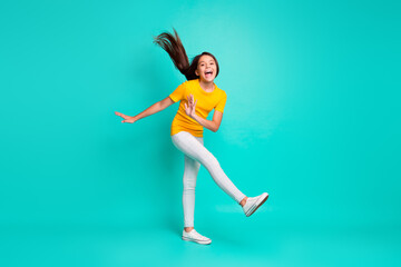 Fototapeta na wymiar Full size photo of funky kid girl with her hair flying feel excited raise leg isolated over turquoise color background