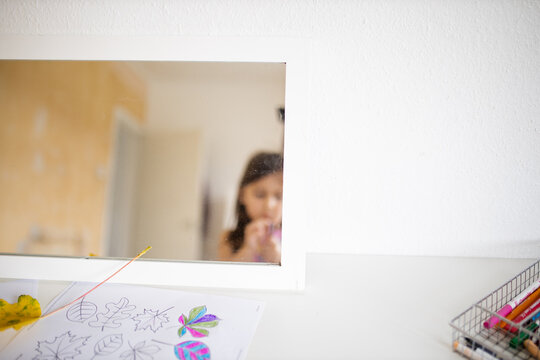 Mirror on a white table reflecting a little girl and a white open door