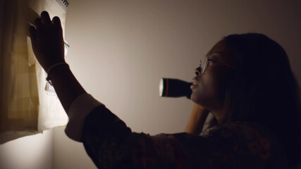 Young african woman with flashlight looking into distribution board