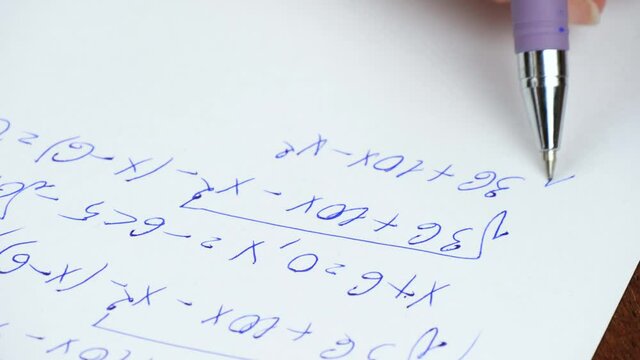 A close-up hand writes mathematical formulas on white paper with a fountain pen.