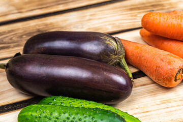 Eggplants, carrots and cucumbers on a wooden background.