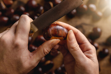 Close up point of  view from the top with woman holding a knife cutting chestnut too cook on the fire. Wooden background. Plenty, autumn, taste concept.