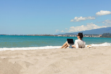 Young woman using laptop computer on a beach. Vacation lifestyle communication. Freelance work concept