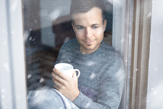 Man with a cup in his hand sitting at a window during winter