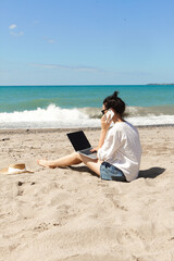 Young woman using laptop computer and talking on the phone on a beach. Vacation lifestyle communication. Freelance work concept