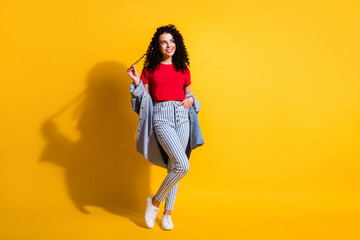 Fototapeta na wymiar Full length photo of pretty girl play curl look up empty space wear red top striped jeans jacket footwear isolated yellow color background
