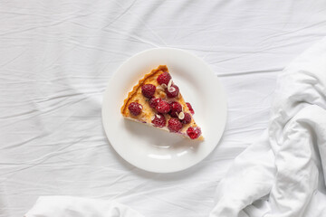 Piece of classic cheesecake with raspberry berries on a white plate on the bed.