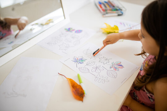 Little girl pointing at a paper sheet with coloring leaves images with a pen