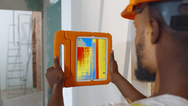 Close up of african professional worker doing analysis of heat on wall with thermal imaging camera
