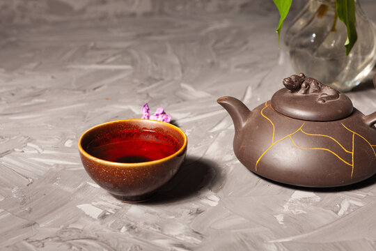 Chinese tea. Tea bowl and teapot on a dark background. Lilac flowers in a vase