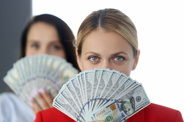 Portrait of two women holding fan of 100 dollar bills in front of their face. Technological schemes in business concept.