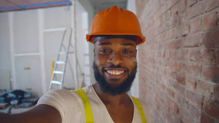 Pov shot of african builder in safety helmet taking selfie over construction site background