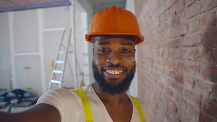 Pov shot of african builder in safety helmet taking selfie over construction site background