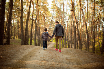 Warm. Father and son walking and having fun in autumn forest, look happy and sincere. Laughting, playing, having good time together. Concept of family, happiness, holidays, childhood, lifestyle.