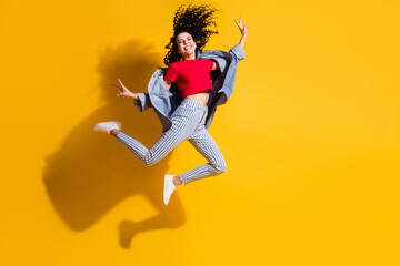 Fototapeta na wymiar Full length photo of girl jump show v-sign wear striped jeans cropped red t-shirt jacket sneakers isolated yellow color background