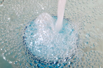 Overflowing water in a blue glass, full overflow glass with water and bubbles