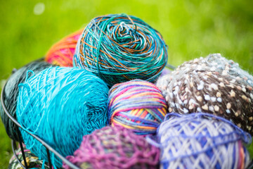Colorful balls of woolen yarn in a metal basket on the grass