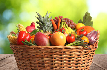Fototapeta na wymiar Fresh organic fruits and vegetables in wicker basket on wooden table, closeup