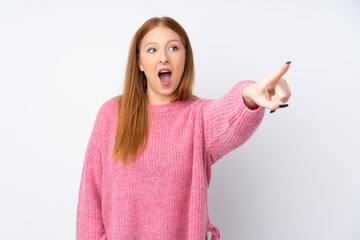 Young redhead woman with pink sweater over isolated white background pointing away