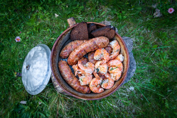 fried sausages, prawns, bread in a pan in the grass