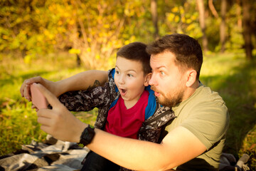 Selfie. Father and son walking and having fun in autumn forest, look happy and sincere. Laughting, playing, having good time together. Concept of family, happiness, holidays, childhood, lifestyle.