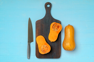 Small pumpkin cut into halves on wooden cutting board with knife