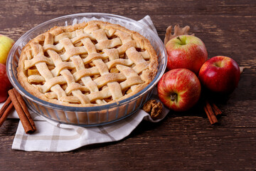 Traditional American Thanks Giving pie with whole organic apples, cinnamon sticks on wooden table. Homemade fruit tart baked to golden crust. Close up, copy space, top view, background.