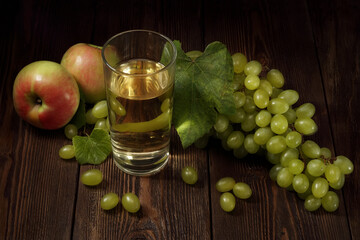 Glass of fresh fruit juice, bunch of sweet green grape and apples on wooden table.