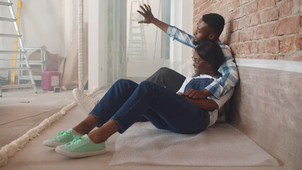 Cheerful black couple talking planning renovation and interior design sitting on floor