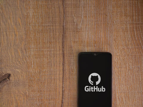 Lod, Israel - July 8, 2020: GitHub app launch screen with logo on the display of a black mobile smartphone on wooden background. Top view flat lay with copy space.