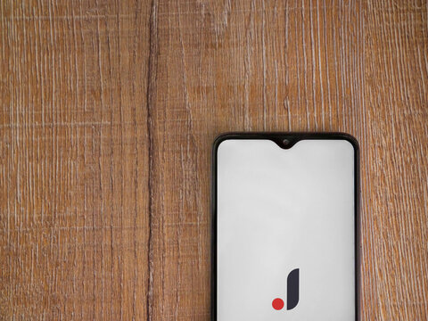 Lod, Israel - July 8, 2020: Joom app launch screen with logo on the display of a black mobile smartphone on wooden background. Top view flat lay with copy space.