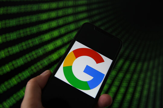 Viersen, Germany - July 9. 2020: View on mobile phone with google logo hold by hand. Screen with tunnel of binary code numbers background.(selective focus on logo)