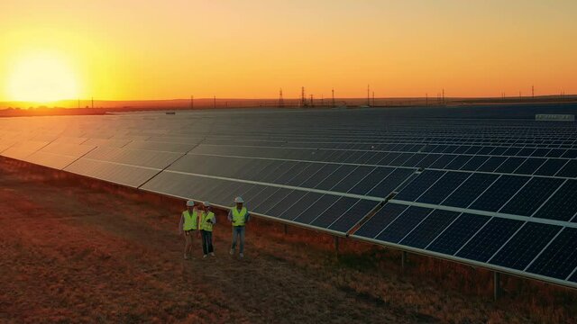 Aerial zoom out shot of workers walking about solar farm at sunset