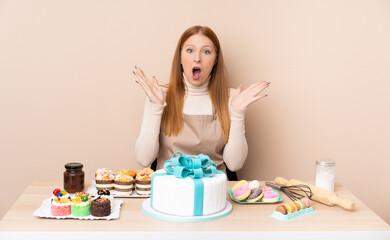 Obraz na płótnie Canvas Young redhead woman with a big cake with surprise facial expression