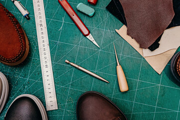 Ruler, awl, knife, paint and leather. Green background top view copy space