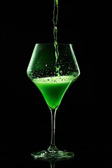 Green drink is poured into a glass. Black background.